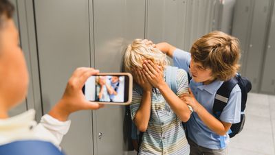 Ein Junge filmt mit seinem Handy, wie ein Junge von einem anderen Jungen in der Schule geärgert wird.