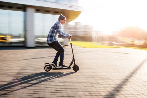Ein Mann fährt mit einem E-Roller bei Sonnenschein über einen gepflasterten Platz