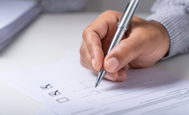 Eine menschliche Hand hält einen Kugelschreiber und füllt ein Formular aus, das vor ihr liegt.