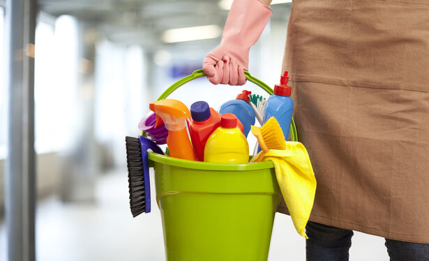 Ein Mensch hat Handschuhe an und trägt in der rechten Hand einen Eimer mit mehreren Putzartikeln
