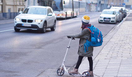 Ein Mädchen mit dem Roller möchte eine Straße überqueren