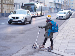 Ein Mädchen mit dem Roller möchte eine Straße überqueren