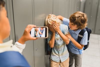 Ein Junge filmt mit seinem Handy, wie ein Junge von einem anderen Jungen in der Schule geärgert wird.
