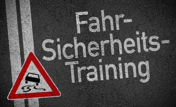 Auf einer Straße steht in weißer Kreide "Fahrsicherheitstraining". Daneben ist ein rotes Dreieck mit einem schleudernden Auto abgebildet.