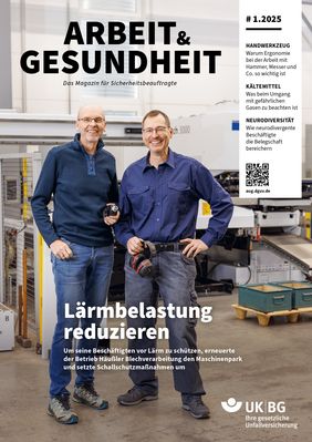 Zwei Männer stehen nebeneinander in einer Werkstatt und schauen lachend in eine Kamera.