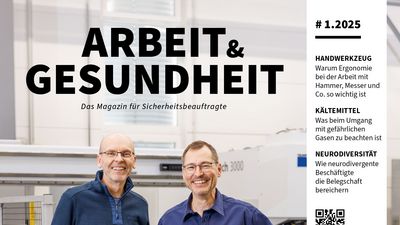 Zwei Männer stehen nebeneinander in einer Werkstatt und schauen lachend in eine Kamera.