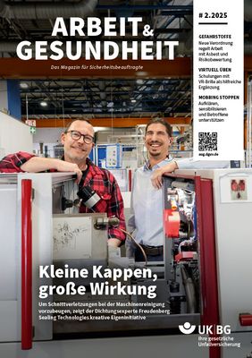 Zwei Männer stehen hinter einer Maschine und lachen in die Kamera