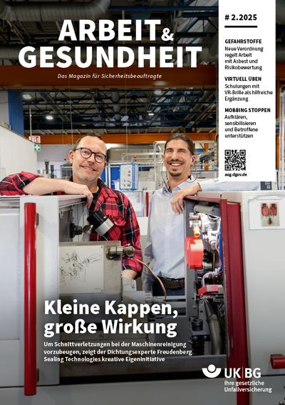 Zwei Männer stehen hinter einer Maschine und lachen in die Kamera