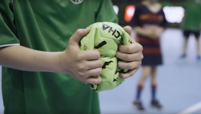 Ein Kind mit einem dunkelgrünen T-Shirt hält einen zerknautschten grünen Ball in den Händen.