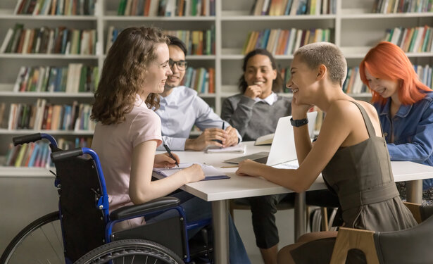 Fünf Jugendliche, davon sitzt ein Mädchen im Rollstuhl, sitzen lachend an einem Tisch