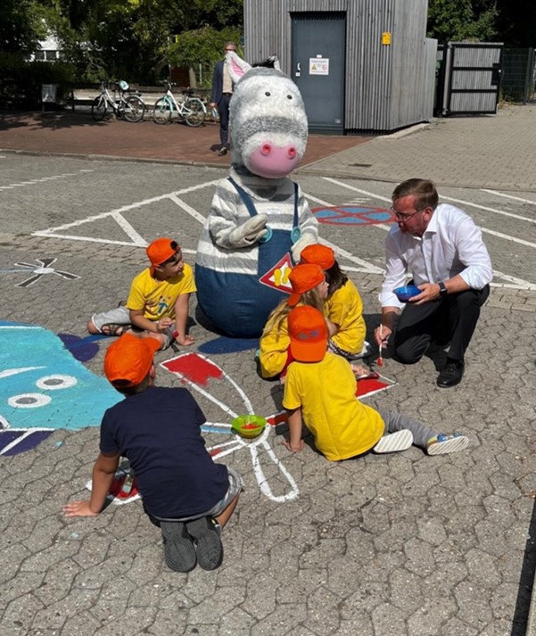 Schulkinder, Minister Pistorius und Moskottchen beim Bemalen des Schulhofparkplatzes